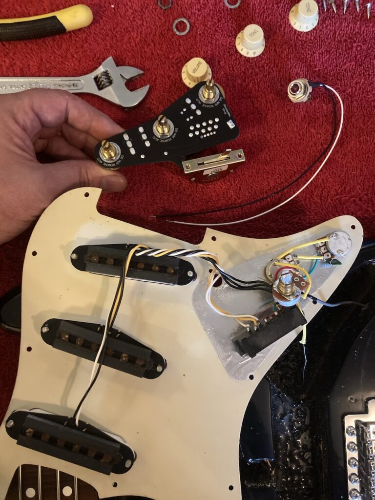 The old potentiometers and switch, still mounted to the underside of the pick-guard, and the new, plate-mounted parts above them (seen from the top), with the new output jack alongside